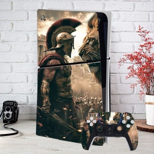 May include: A white and black games console with a custom skin depicting a Spartan warrior and a lion. The matching controller has a similar design. The console is set against a white brick wall.