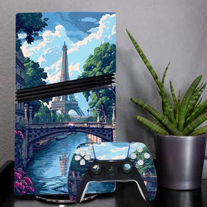 May include: A video game console and controller featuring a scenic illustration of Paris, including the Eiffel Tower, a bridge, and a river. The controller has a matching design. A potted plant is to the right.
