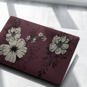May include: A laptop computer with a burgundy floral design. The design features white flowers with black outlines and black leaves on a burgundy background.