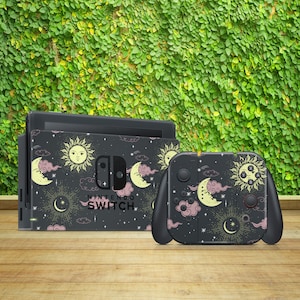 May include: A black Nintendo Switch console and controller with a custom skin featuring a celestial design. The design includes moons, stars, and suns in shades of yellow, pink, and white on a dark background. The text "Nintendo Switch" is printed on the console.