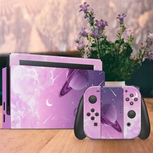 Può includere: Una console e un controller Nintendo Switch di colore viola e rosa con un design a galassia. Il design presenta un pianeta con anelli, stelle e stelle cadenti.