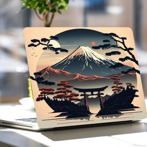 May include: A laptop with a colorful sticker featuring a mountain range, a red sun, and a traditional Japanese gate. The sticker is in a circle with a dark blue background and a light beige border.