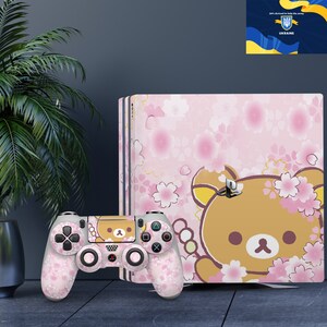 May include: A pink and white PlayStation 4 console with a cherry blossom and bear design. The console is next to a matching pink and white controller.