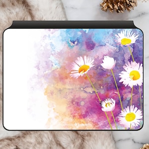 Può includere: Un'illustrazione ad acquerello di margherite bianche con centri gialli su uno sfondo di lavaggi ad acquerello rosa, viola e blu.