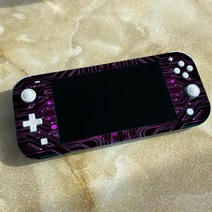 May include: A black and purple Nintendo Switch Lite console with a circuit board design. The console has white buttons and a black screen.