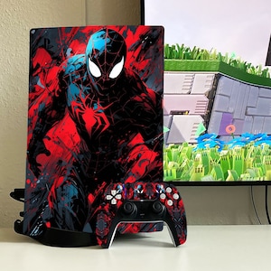 May include: A black and red video game console with a Spiderman design. The console is on a white surface with a black controller.