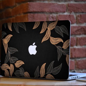 May include: Black laptop with a gold and white leaf design on the cover. The Apple logo is visible on the cover.