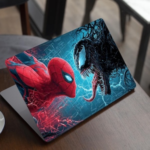 Pode incluir: Skin para laptop com uma ilustração vibrante do Homem-Aranha contra Venom. O design mostra os personagens em poses dinâmicas sobre um fundo azul e vermelho com efeitos de raios. O laptop está em uma mesa de madeira.