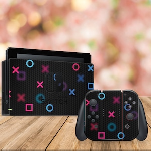 May include: A black Nintendo Switch console and controller with a black and white geometric pattern featuring pink, blue, and cyan circles, squares, and X's.