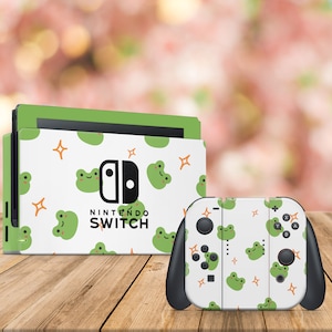 Può includere: Una console e un controller Nintendo Switch bianchi con un motivo a rana verde e stelle. Il testo "Nintendo Switch" è stampato sulla console.