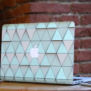 May include: A laptop computer with a geometric pattern on the lid. The pattern is made up of light blue and white triangles. The laptop is sitting on a wooden table.