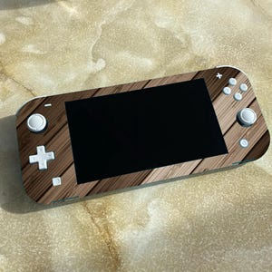 Op de afbeelding: Een bruine en witte Nintendo Switch Lite console met een houtnerf ontwerp. De console heeft een zwart scherm en witte knoppen.