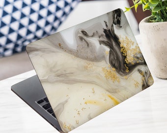 May include: Laptop with a decorative cover featuring a swirling abstract design in shades of grey, black, and cream, accented with gold glitter. The laptop is open on a white surface.