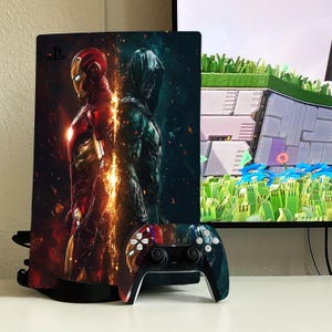 May include: A black PlayStation 5 console with a custom skin featuring Iron Man and Green Arrow. The console is standing upright on a white surface. A black PlayStation 5 controller is in front of the console.