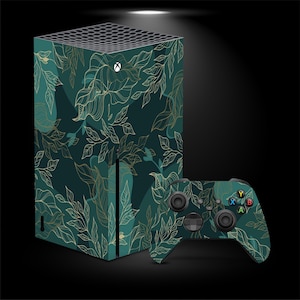 Peut inclure: Une console Xbox Series X et une manette assortie présentent un motif de feuilles vert d'eau et dorées. La console est verticale, la manette est à droite. Le design présente un fond vert foncé avec des contours de feuilles dorées.