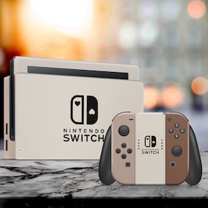Peut inclure: Une console Nintendo Switch beige avec un logo Nintendo Switch noir et le texte "NINTENDO SWITCH" sur le devant. La console est à côté d'une manette Nintendo Switch Joy-Con beige et marron avec le texte "NINTENDO SWITCH" sur le devant.