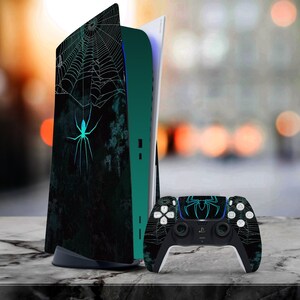 May include: A black and green PlayStation 5 console with a spider web and spider design. The console is next to a black PlayStation 5 controller with a spider web and spider design.