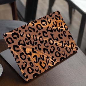 May include: A laptop computer with a brown and black leopard print skin. The skin has a gold glitter effect.
