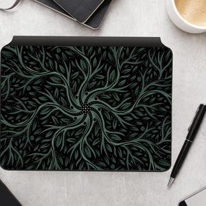 May include: Black and green decorative tablet cover featuring a symmetrical botanical design. The pattern includes stylized leaves and branches radiating from a central point. The cover has a black border and is on a desk.