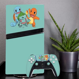 Può includere: Una console di gioco e un controller turchese con una grafica di tre personaggi dei cartoni animati. La console e il controller sono su una superficie nera, con una pianta in vaso sullo sfondo.