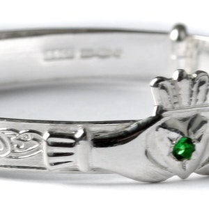 May include: A silver Claddagh bangle with a green stone in the heart. The bangle is decorated with Celtic knotwork.