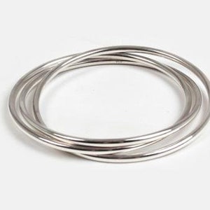 May include: Four silver bangles stacked on top of each other. The bangles are smooth and shiny.