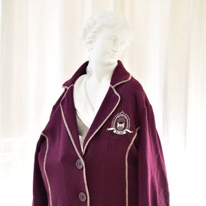 Puede incluir: Una chaqueta de color burdeos con ribetes de color crema y un parche en el pecho izquierdo con el texto "Australian College of Physical Education" y "For the High".