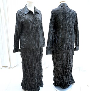 May include: A black two-piece outfit with a long-sleeved collared shirt and a long skirt. Both pieces are made of a crinkled fabric.