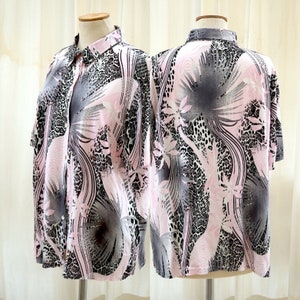 Pode incluir: Uma camisa de botão de manga curta rosa, preta e branca com estampa tropical. A camisa tem gola e fechamento de botões.