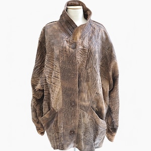 Puede incluir: Una chaqueta de cuero marrón con cuello alto y cierre de botones. La chaqueta tiene un aspecto texturizado y desgastado y presenta dos bolsillos con solapa.