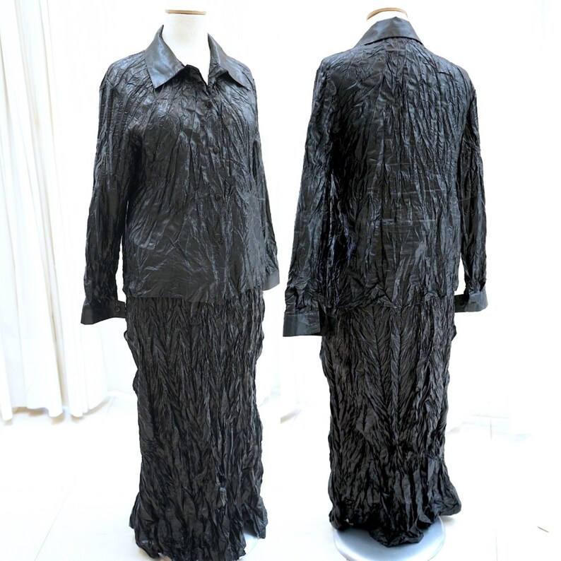 May include: A black two-piece outfit with a long-sleeved collared shirt and a long skirt. Both pieces are made of a crinkled fabric.