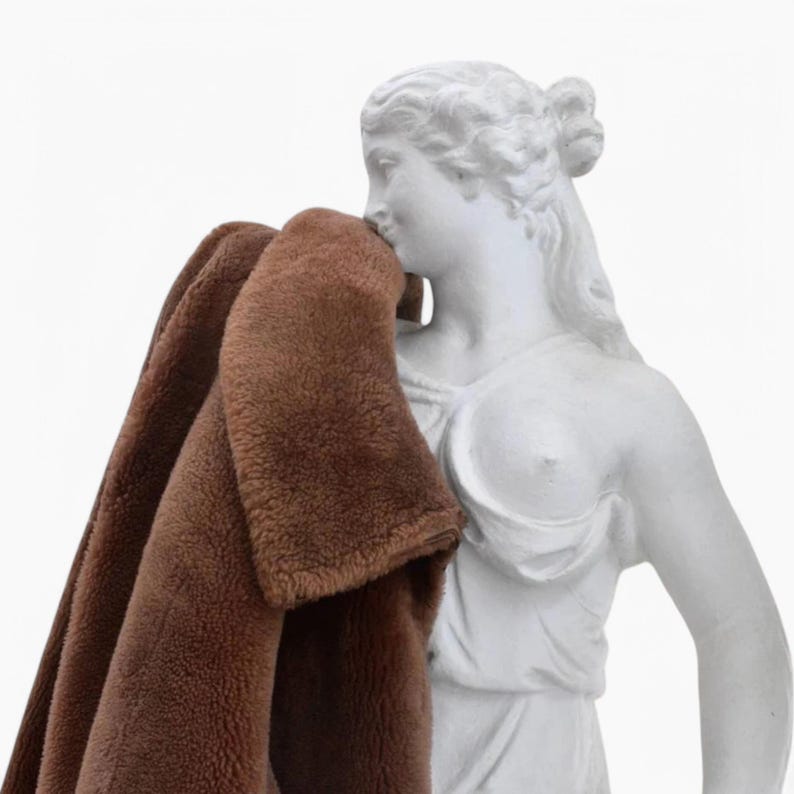 K&ouml;nnte beinhalten: Eine wei&szlig;e Gipsstatue einer Frau mit einem braunen Kunstfell&uuml;berwurf &uuml;ber den Schultern.