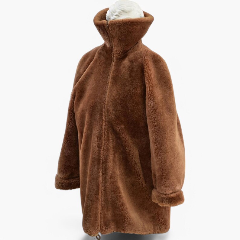K&ouml;nnte beinhalten: Eine braune Schaffelljacke mit Rei&szlig;verschluss. Die Jacke hat einen hohen Kragen und lange &Auml;rmel.