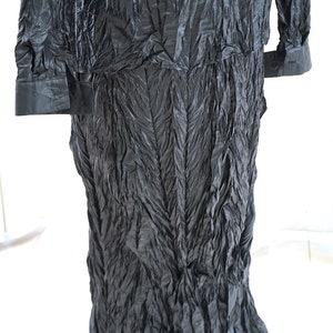 May include: A black long-sleeved shirt with a crinkled texture. The shirt has a collar and long sleeves with button cuffs. The shirt is made of a soft, flowing fabric.