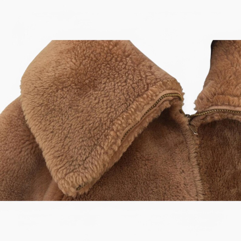 K&ouml;nnte beinhalten: Nahaufnahme einer braunen Kunstfelljacke mit Rei&szlig;verschluss. Die Jacke hat eine weiche, pl&uuml;schige Textur und einen hohen Kragen.