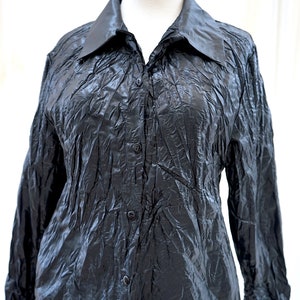 May include: A black long-sleeved button-down shirt with a crinkled texture. The shirt has a collared neckline and a button closure.