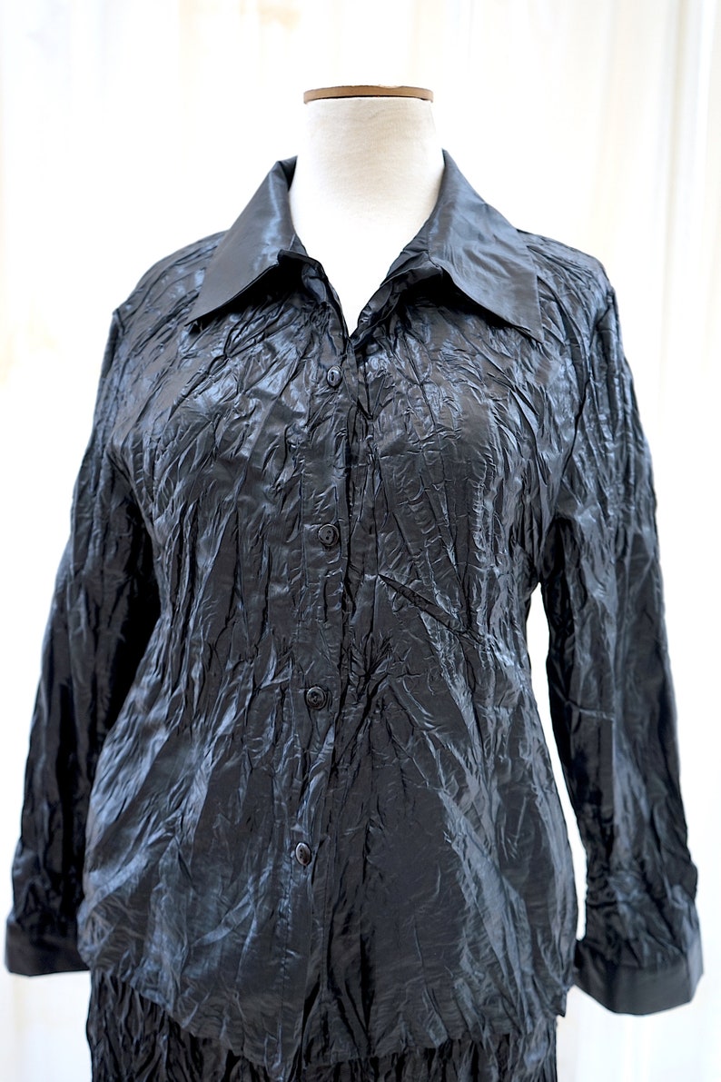 May include: A black long-sleeved button-down shirt with a crinkled texture. The shirt has a collared neckline and a button closure.