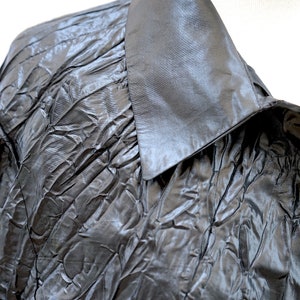 May include: A black, crinkled, satin blouse with a large, pointed collar.