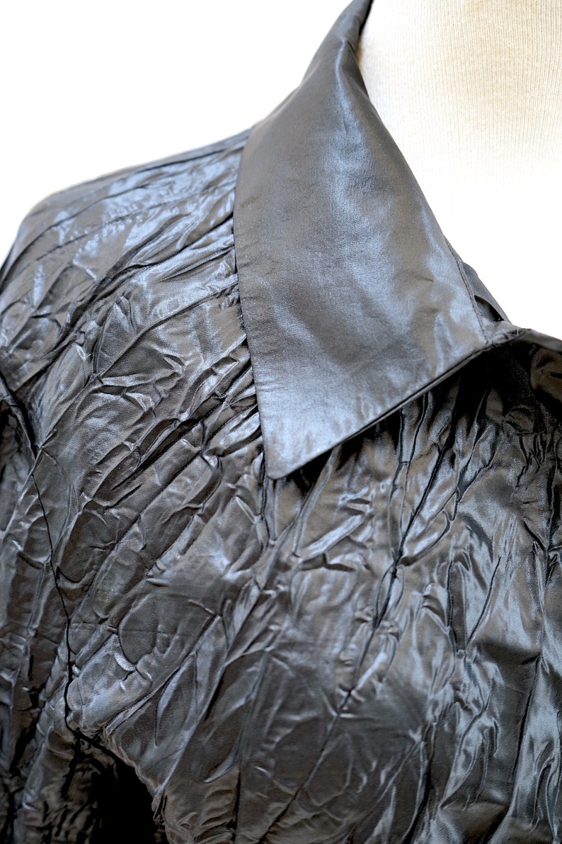 May include: A black, crinkled, satin blouse with a large, pointed collar.