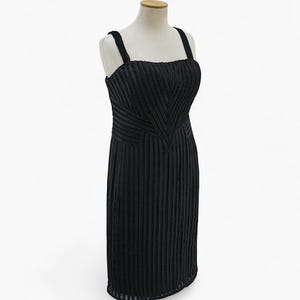 May include: A black, knee-length dress with a square neckline and thick straps. The bodice features a chevron design, and the skirt has vertical pleats. The dress is displayed on a mannequin.