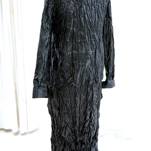 May include: A long black dress with a crinkled texture. The dress has a collar and long sleeves.
