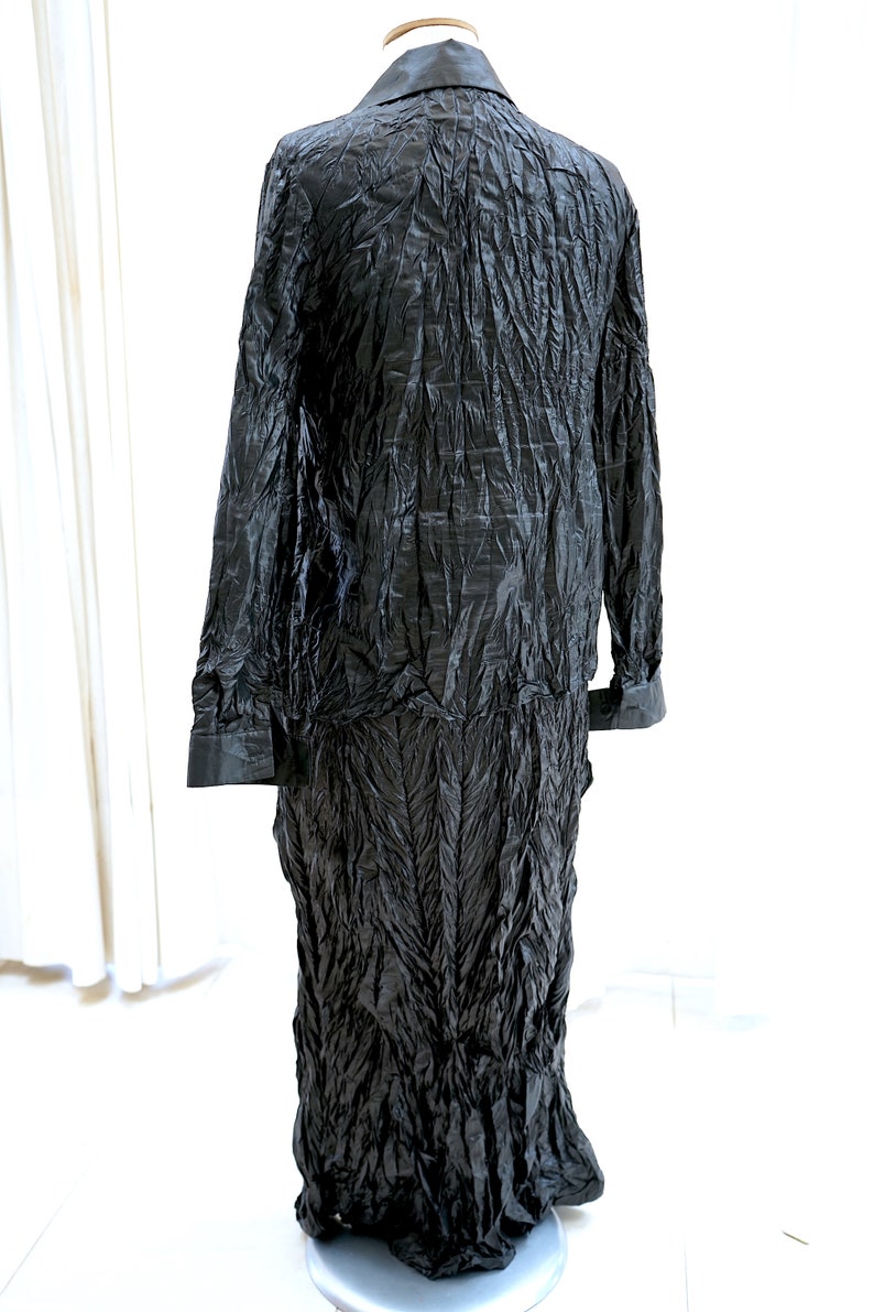 May include: A long black dress with a crinkled texture. The dress has a collar and long sleeves.