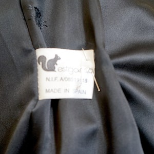 K&ouml;nnte beinhalten: Nahaufnahme eines schwarzen Stoffes mit einem Etikett. Das Etikett zeigt ein Eichh&ouml;rnchen-Logo und den Text "estgar sa", sowie "N.I.F. A08512118" und "MADE IN SPAIN".
