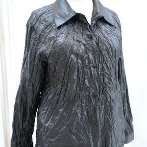 May include: A black long-sleeved shirt with a collared neckline and button closure. The shirt is made of a crinkled fabric.
