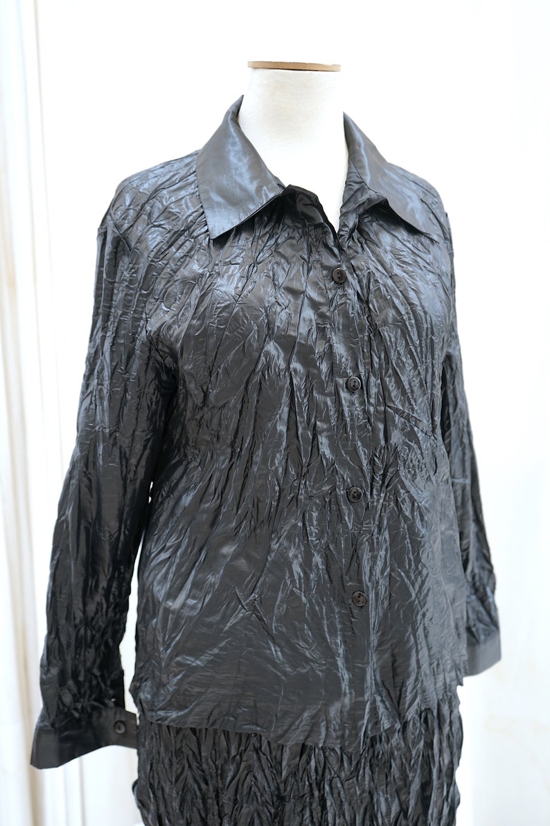 May include: A black long-sleeved shirt with a collared neckline and button closure. The shirt is made of a crinkled fabric.
