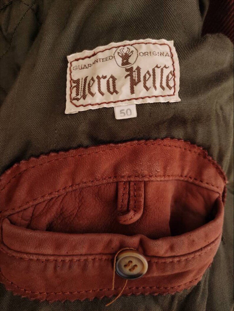 Puede incluir: Un bolsillo de parche de cuero marr&oacute;n con un bot&oacute;n en una chaqueta verde. La chaqueta tiene una etiqueta que dice "Guaranteed Original Vera Pelle" y "50".