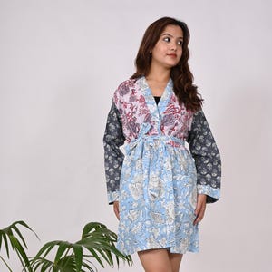May include: A patterned robe in shades of blue, pink, and gray. The robe features a floral design and a tie at the waist. The sleeves are long and the robe falls to mid-thigh. A potted plant is in the background.