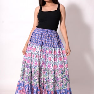 Puede incluir: Una falda larga escalonada con estampado floral en tonos azules, rosas y blancos. La falda se combina con una camiseta sin mangas negra. El diseño de la falda presenta una mezcla de estampados florales y un dobladillo con volantes, creando un estilo bohemio.