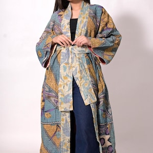 May include: A long, patterned kimono in shades of blue, gold, and purple. The kimono features a belt and a floral and geometric design. The sleeves are wide, and the garment is worn over dark blue jeans and a black top.