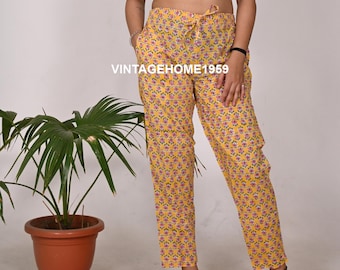 May include: Yellow floral print trousers with a drawstring waist and pockets. The trousers feature a repeating pattern of pink flowers. The text "VINTAGEHOME1959" is visible. The trousers are worn with a black crop top.